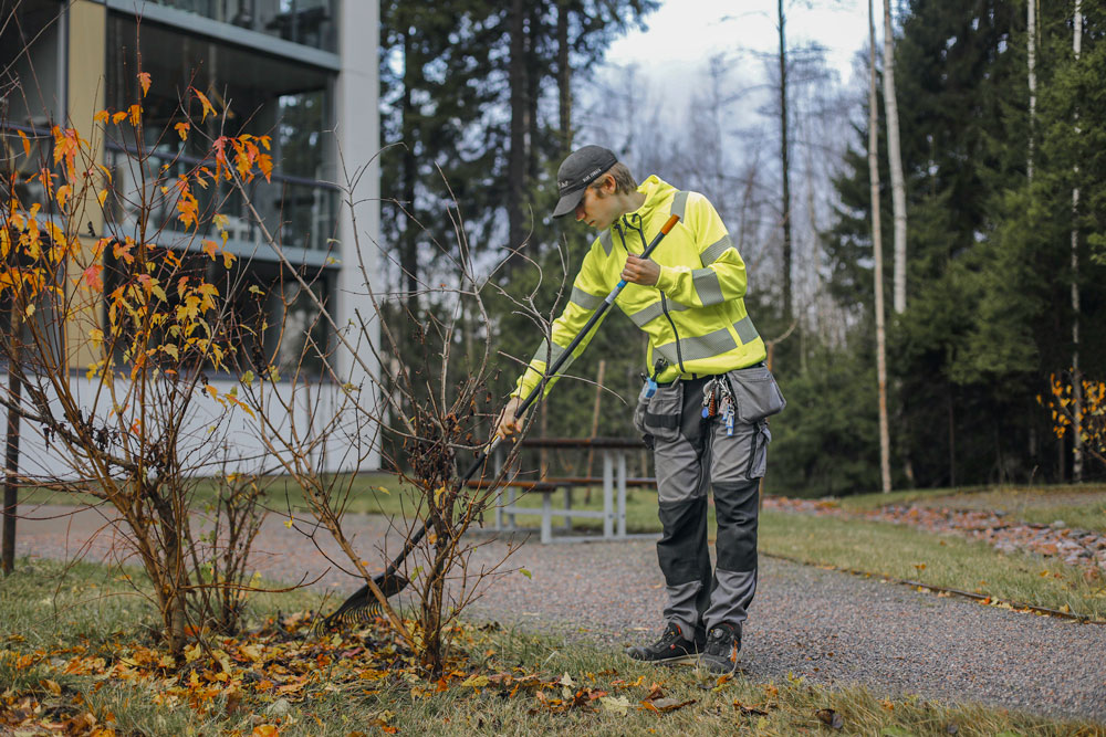 Kiinteistöhuollon työntekijä haravoi lehtiä kiinteistön pihalla syksyllä.
